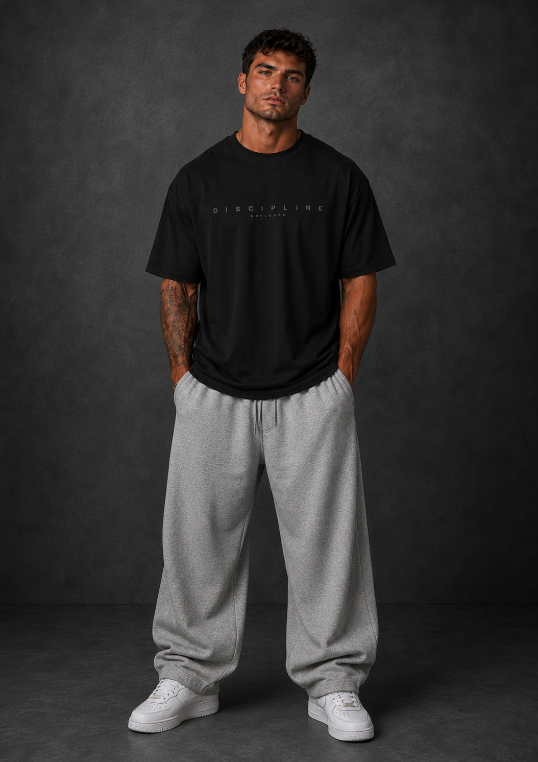 Man wearing a black gym pump cover t-shirt with text and gray sweatpants on a dark background